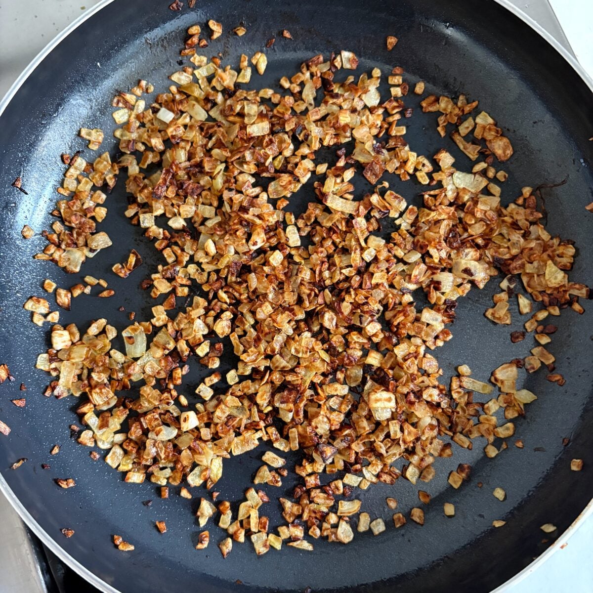 Diced onions are browning and caramelizing in a black frying pan.