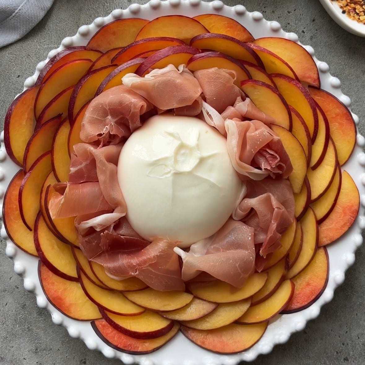 A white plate with overlapping slices of nectarine, layered with prosciutto, and a ball of burrata cheese in the center.