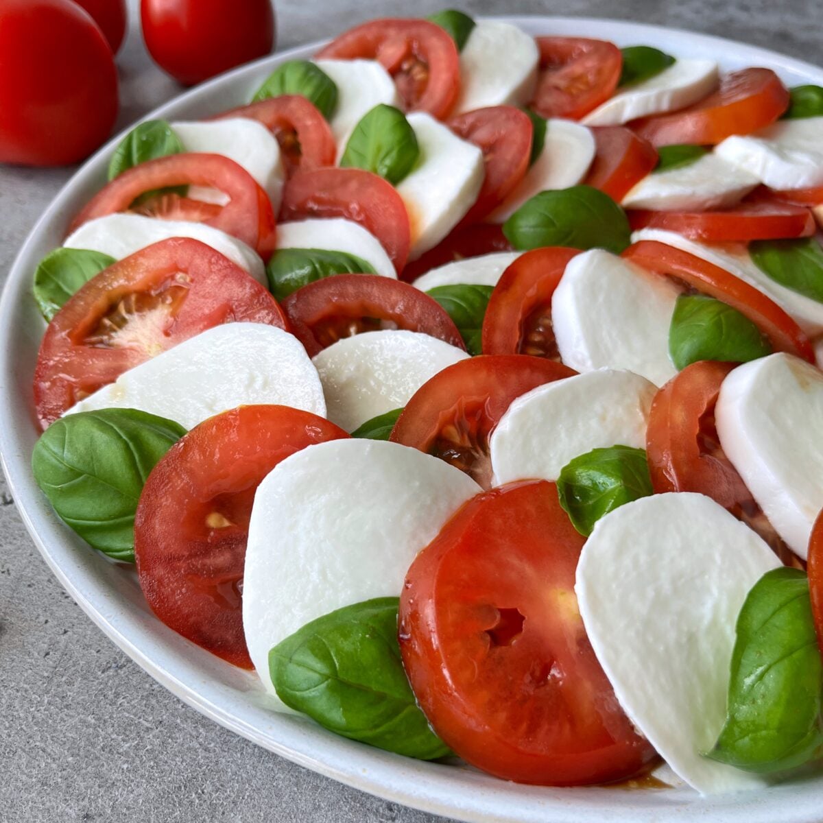 A side view of a Tomato Caprese Salad featuring alternating slices of tomato, mozzarella cheese, and fresh basil leaves arranged in a beautiful circular pattern.