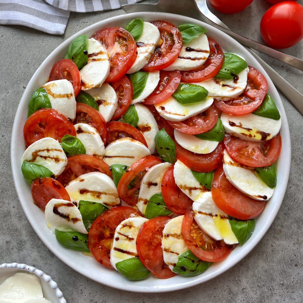 A plate of sliced tomatoes, mozzarella cheese, and fresh basil leaves arranged in a circular pattern, drizzled with balsamic glaze.