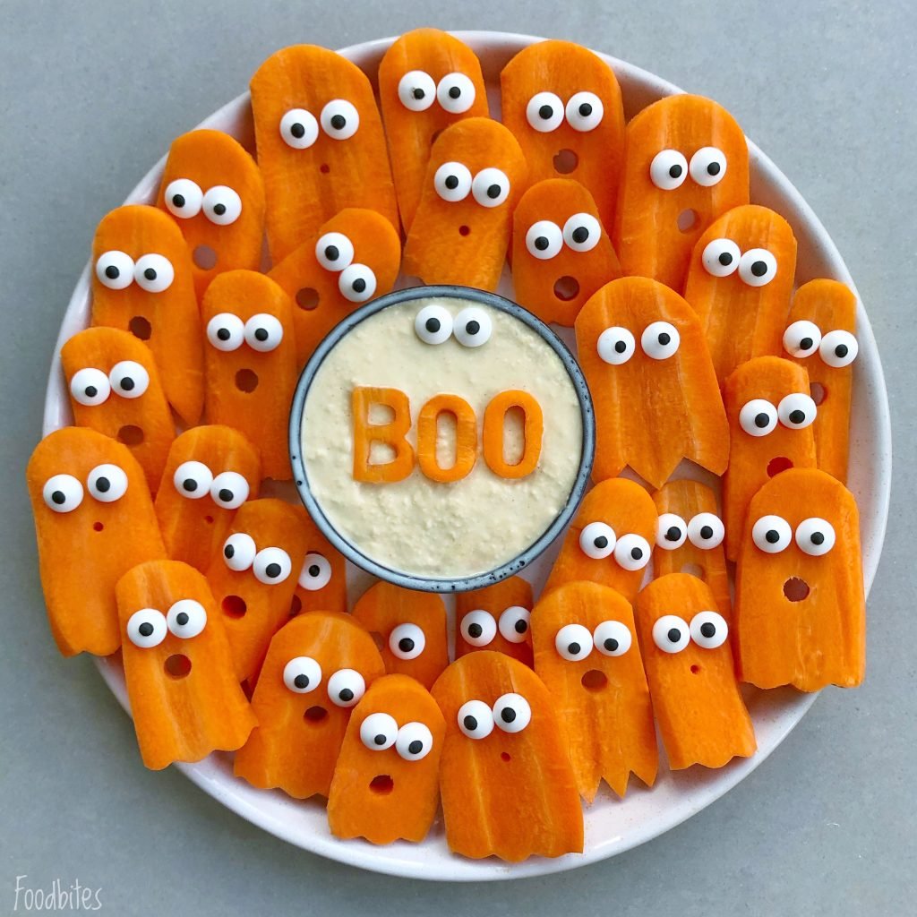 A plate of carrot slices shaped like ghosts topped with candy eyes surrounds a bowl of dip. This fun dish features the word “BOO” spelled out with carrot letters in the center.