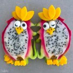 Two halved dragon fruits decorated to look like cartoon owls with mango slices for crests and feet, candy eyes, and small fruit pieces for beaks—these fun bites make creative and healthy dishes for food recipes. Arranged on a gray surface.