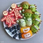 A plate of creatively arranged fruits and veggies makes healthy Halloween bites: watermelon skeletons, kiwi monsters, green apple mummies, blueberry spiders, and bell pepper mouths with teeth.