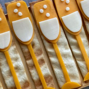 Rectangular crackers topped with cheese and white cheese slices arranged like champagne glasses, with small cheese circles as bubbles—these fun bites are perfect for party food recipes or festive dishes.
