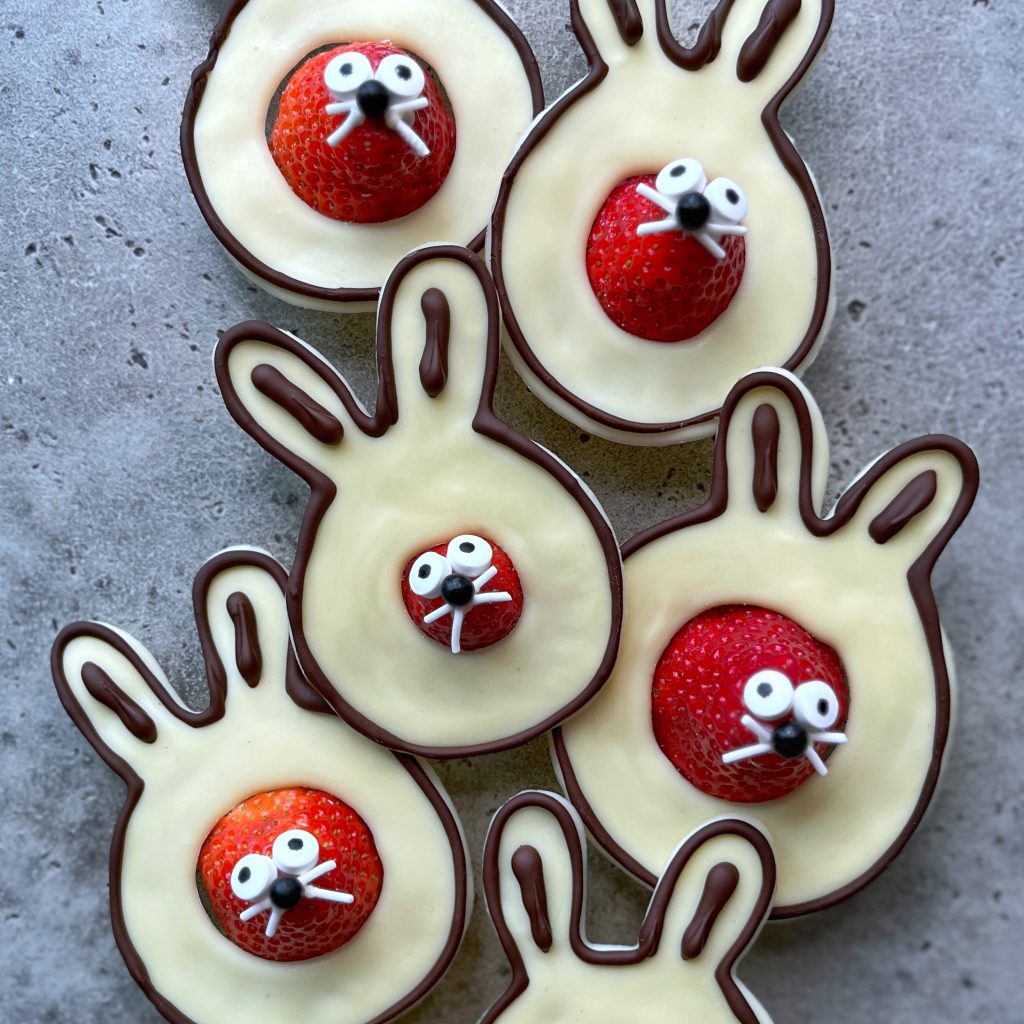 Five bunny-shaped treats made of chocolate with white chocolate filling, each featuring a strawberry for a nose and decorated with candy eyes and white icing for whiskers and teeth—fun, delicious bites perfect for festive food recipes.