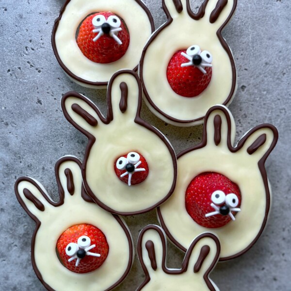 Five bunny-shaped treats made of chocolate with white chocolate filling, each featuring a strawberry for a nose and decorated with candy eyes and white icing for whiskers and teeth—fun, delicious bites perfect for festive food recipes.