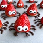 Strawberries decorated with candy eyes and chocolate legs to resemble cute spiders make fun, healthy bites—perfect for creative food recipes and party dishes, arranged on a light surface.