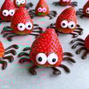 Strawberries decorated with candy eyes and chocolate legs to resemble cute spiders make fun, healthy bites—perfect for creative food recipes and party dishes, arranged on a light surface.