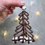 A hand holds a Christmas tree-shaped chocolate decoration with a silver star on top and marshmallows at the base piped with chocolate to look like presents.