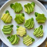 A plate of whimsical avocado bites garnished with fresh basil leaves all arranged neatly on a white ceramic plate.