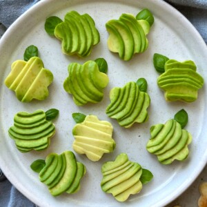 A plate of whimsical avocado bites garnished with fresh basil leaves all arranged neatly on a white ceramic plate.