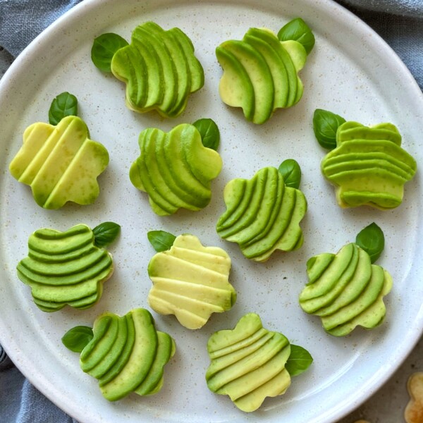 A plate of whimsical avocado bites garnished with fresh basil leaves all arranged neatly on a white ceramic plate.