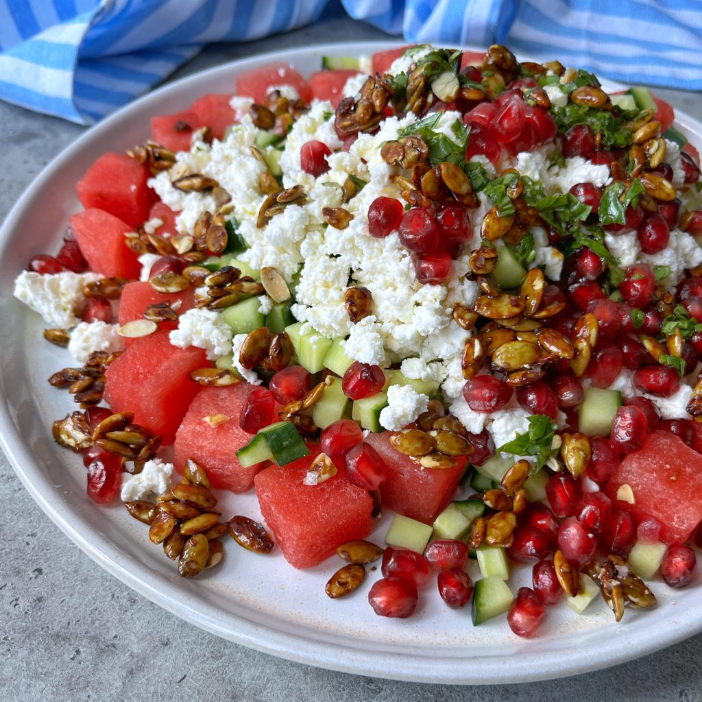 A plate of fresh watermelon, cucumber, and crumbled feta topped with pomegranate seeds, chopped herbs, and caramelized sunflower seeds makes for one of the most refreshing health bites in summer food recipes.