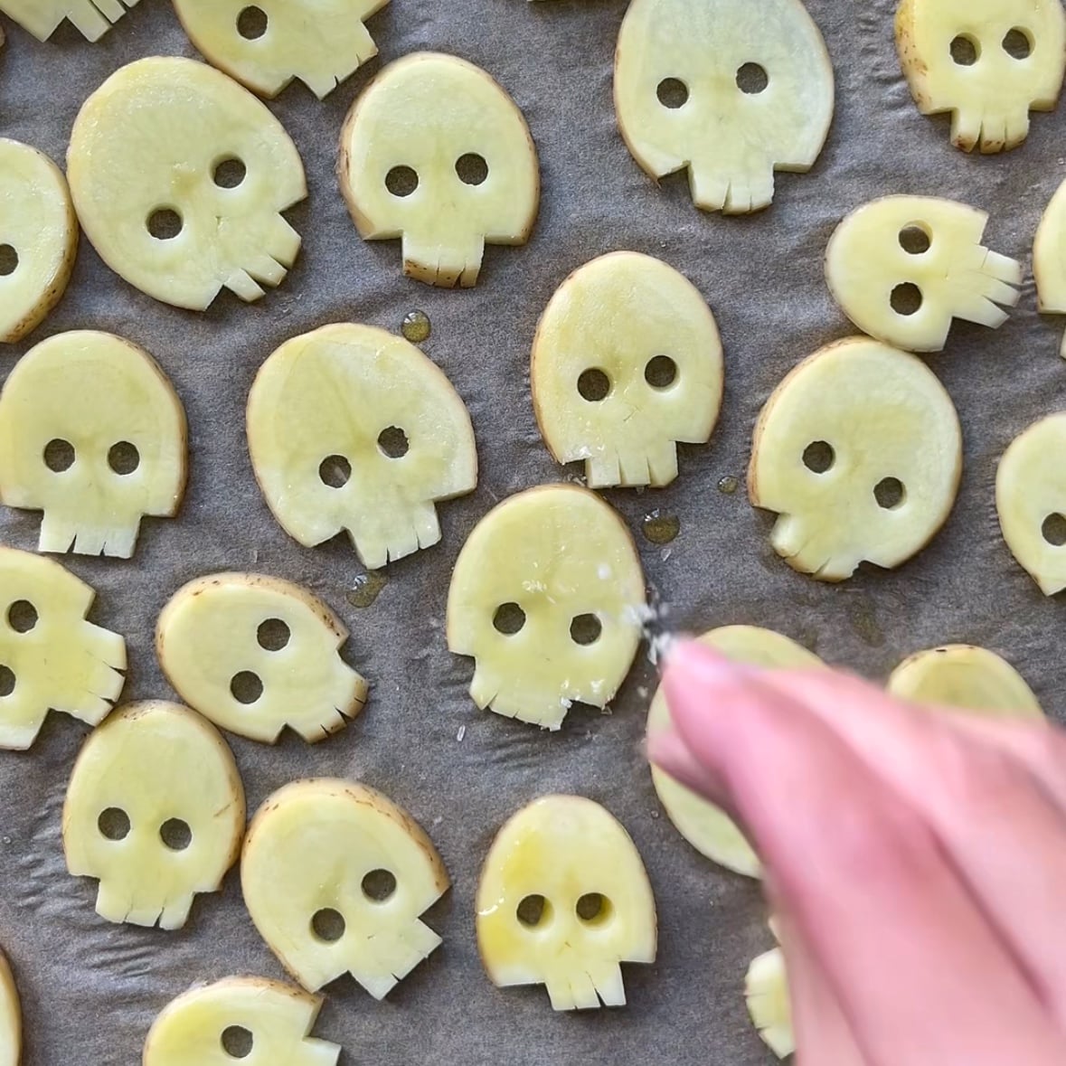 A hand seasons Halloween potato fries on a baking sheet with sea salt.