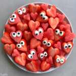 A plate of heart-shaped watermelon and strawberry bites, each topped with candy eyes, arranged to look like cute, playful faces—perfect for fun and healthy food recipes.