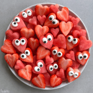 A plate of heart-shaped watermelon and strawberry bites, each topped with candy eyes, arranged to look like cute, playful faces—perfect for fun and healthy food recipes.