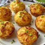 A plate of golden-brown Individual Dauphinoise Potatoes stacked neatly and garnished with chopped green onions. The stacks are crispy on the edges and beautifully arranged on a white plate.