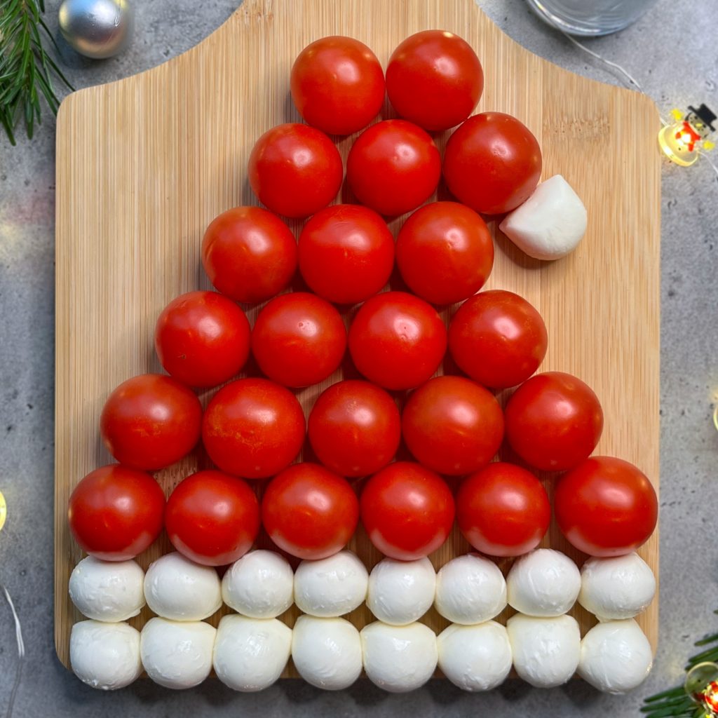 Cherry tomatoes and mozzarella balls are arranged on a wooden board in the shape of a Santa hat.