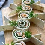 Tortilla pinwheels filled with smoked salmon, cucumber, and cream cheese are arranged on a wooden board.