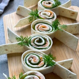 Tortilla pinwheels filled with smoked salmon, cucumber, and cream cheese are arranged on a wooden board.