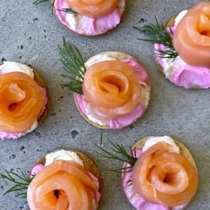 Round crackers topped with swirls of smoked salmon, a pink and white creamy spread, and fresh dill make elegant bites—perfect for health-conscious food lovers seeking delicious recipes to impress on a speckled grey surface.