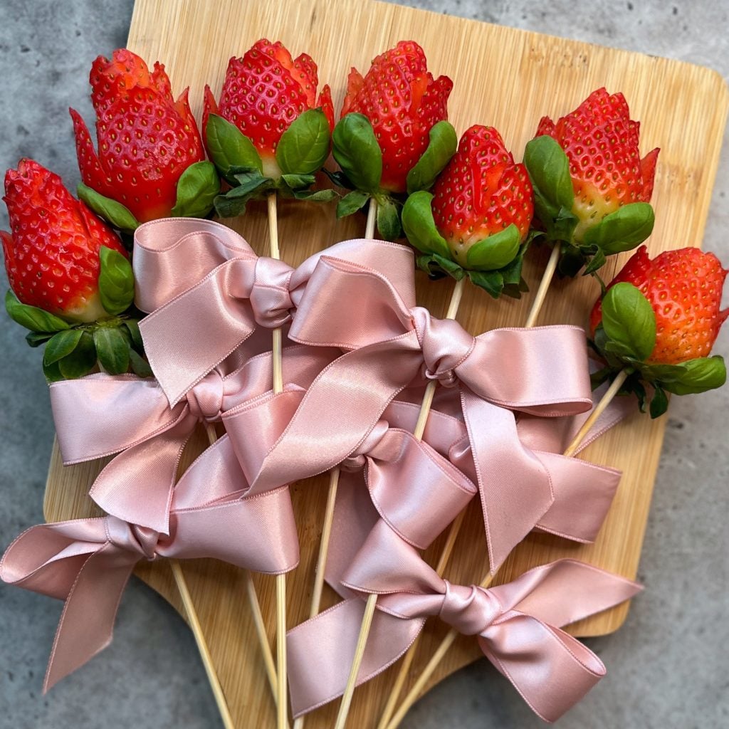 Strawberries carved to look like roses and arranged on skewers with green leaves and tied with large pink satin bows.