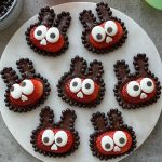 Seven Strawberry Bunnies made with halved strawberries, chocolate ears and borders, large candy eyes, and tiny white candy noses are arranged on a round white plate.