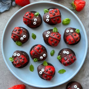A plate of Oreo cookies and chocolate-covered strawberries decorated to look like ladybugs, with candy eyes and chocolate dots, garnished with fresh green basil leaves—perfect for fun party bites or creative food recipes.
