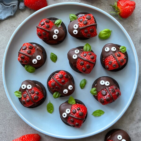 A plate of Oreo cookies and chocolate-covered strawberries decorated to look like ladybugs, with candy eyes and chocolate dots, garnished with fresh green basil leaves—perfect for fun party bites or creative food recipes.