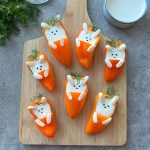 Stuffed Mini Peppers are transformed into adorable bunny faces—orange bell pepper halves filled with creamy white dip, then decorated with dill, black sesame seeds, and marshmallows on a wooden cutting board.