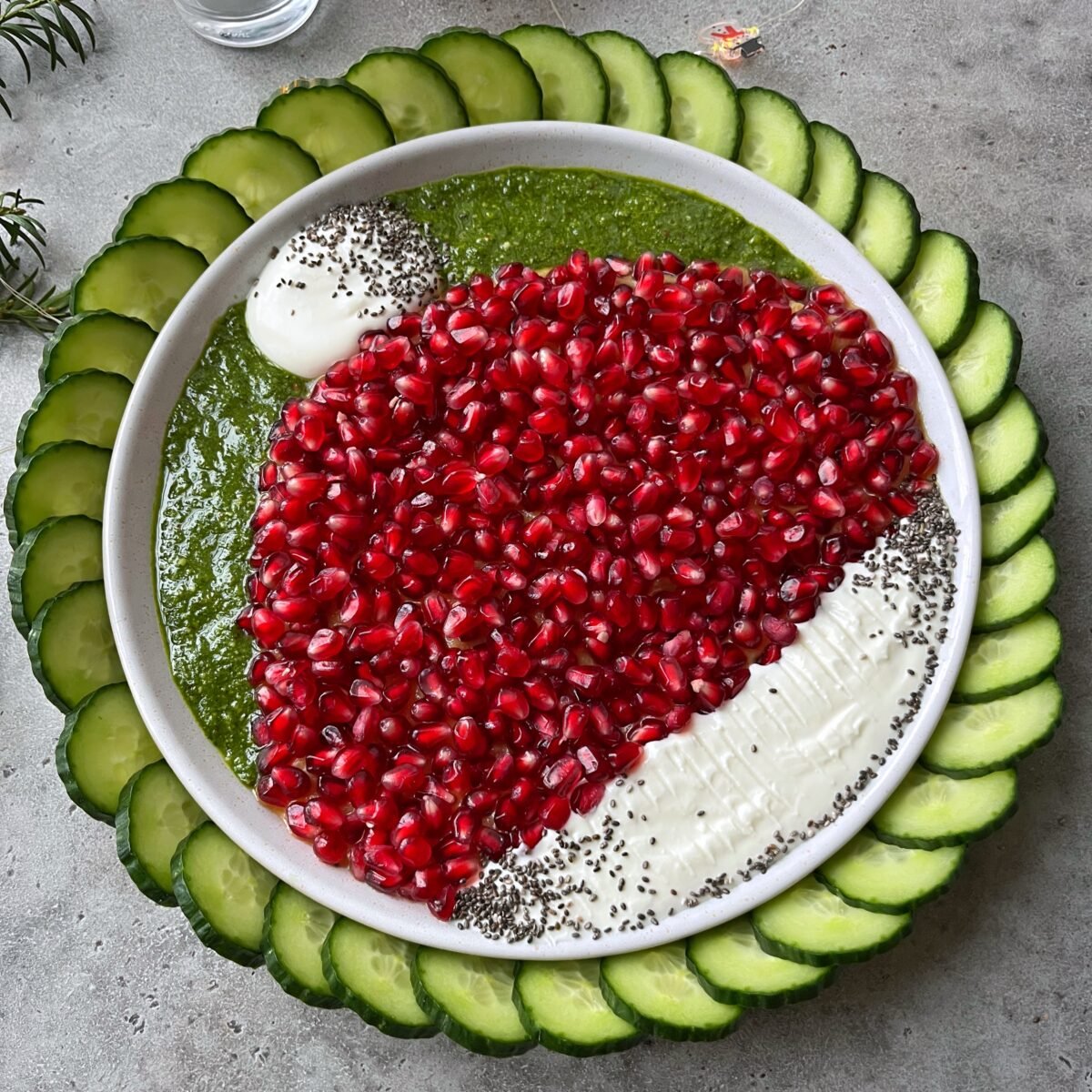 A platter arranged with sliced cucumbers, pesto, whipped feta, chia seeds, and pomegranate seeds forming a design resembling a Santa hat.
