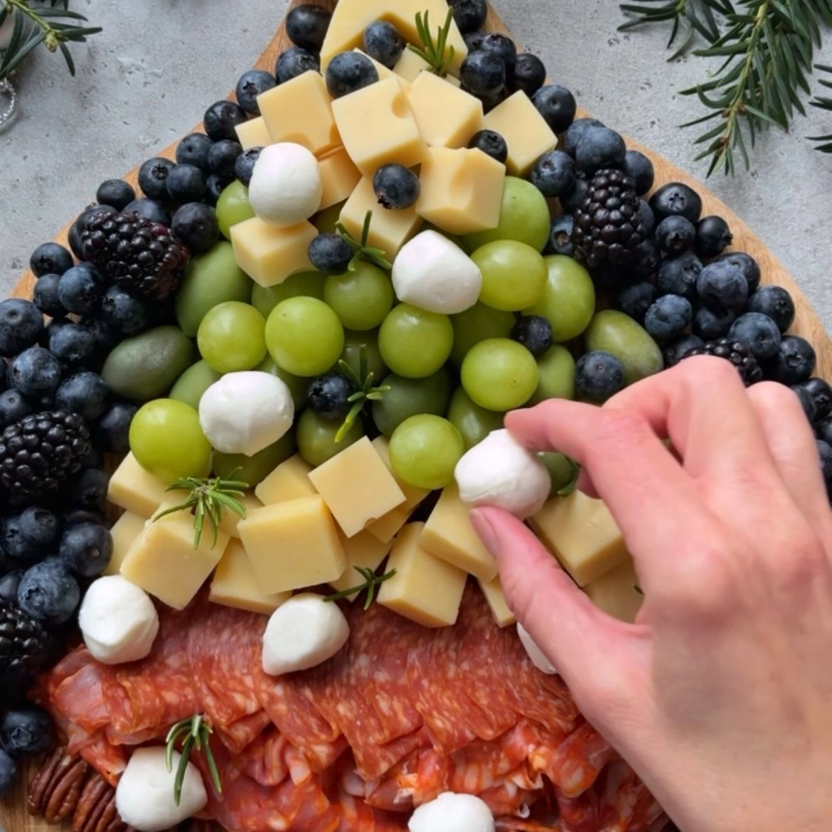 A hand places a mozzarella ball on a Christmas Tree Charcuterie Board.
