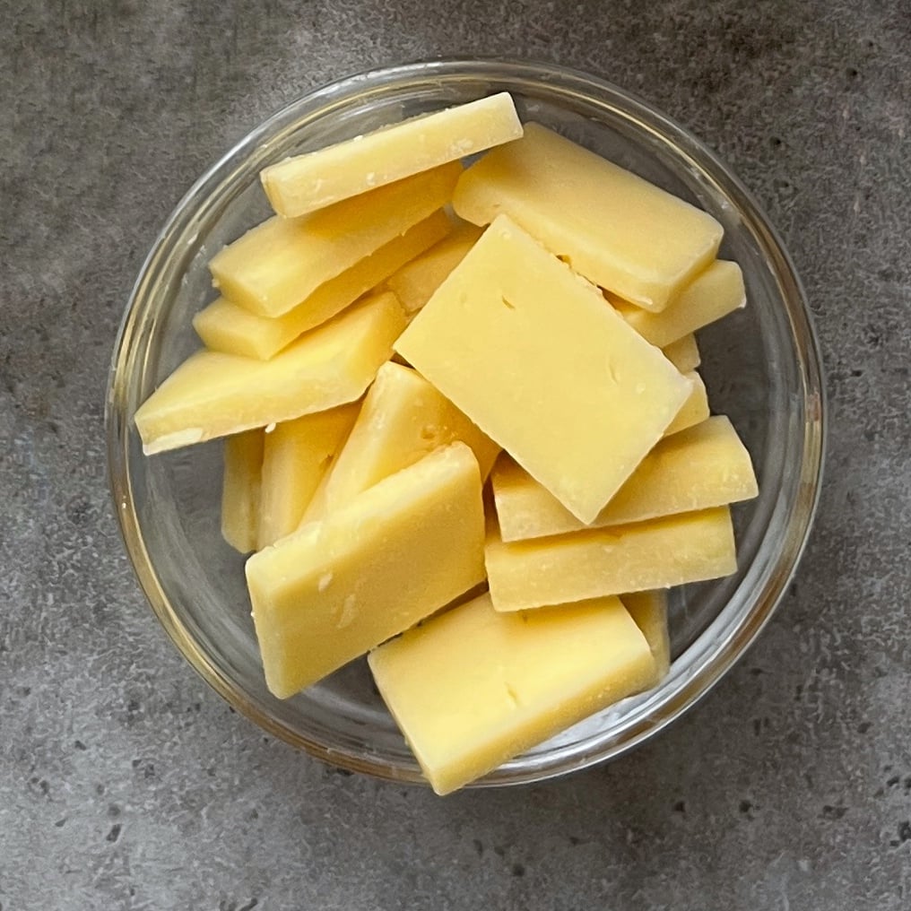 A glass bowl filled with rectangular slices of cheddar cheese.