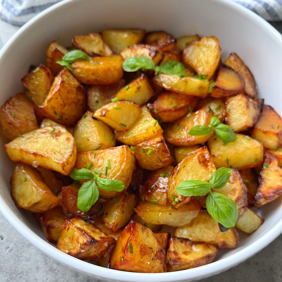 A white bowl filled with roasted potato wedges garnished with fresh green herbs.