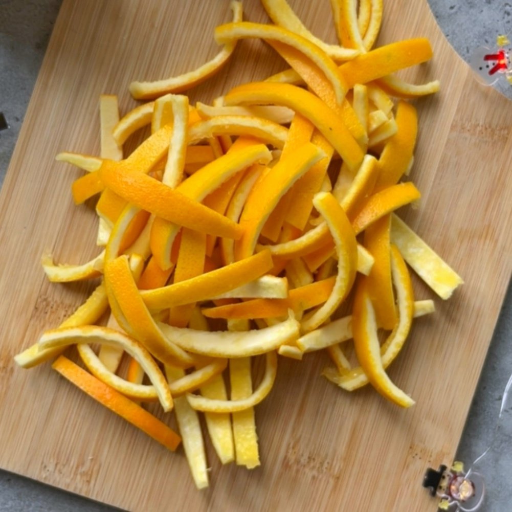 Orange citrus peels sliced into thin strips piled on a wooden cutting board.