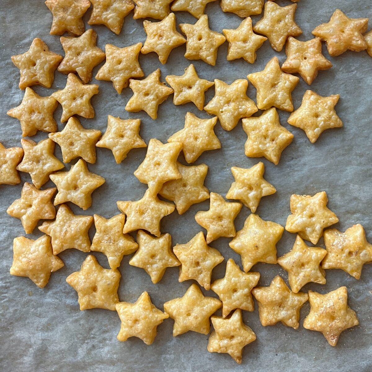 Several small, golden-brown, star-shaped crackers are arranged on a sheet of parchment paper.