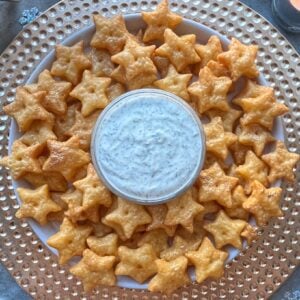 A plate of star-shaped Cheddar Crackers arranged neatly around a bowl of white dipping sauce.