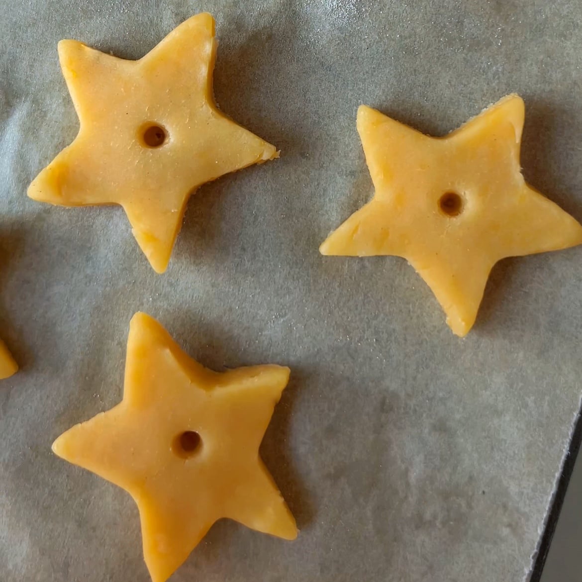 Three uncooked, star-shaped Cheddar Crackers with holes in the center are arranged on a sheet of parchment paper.