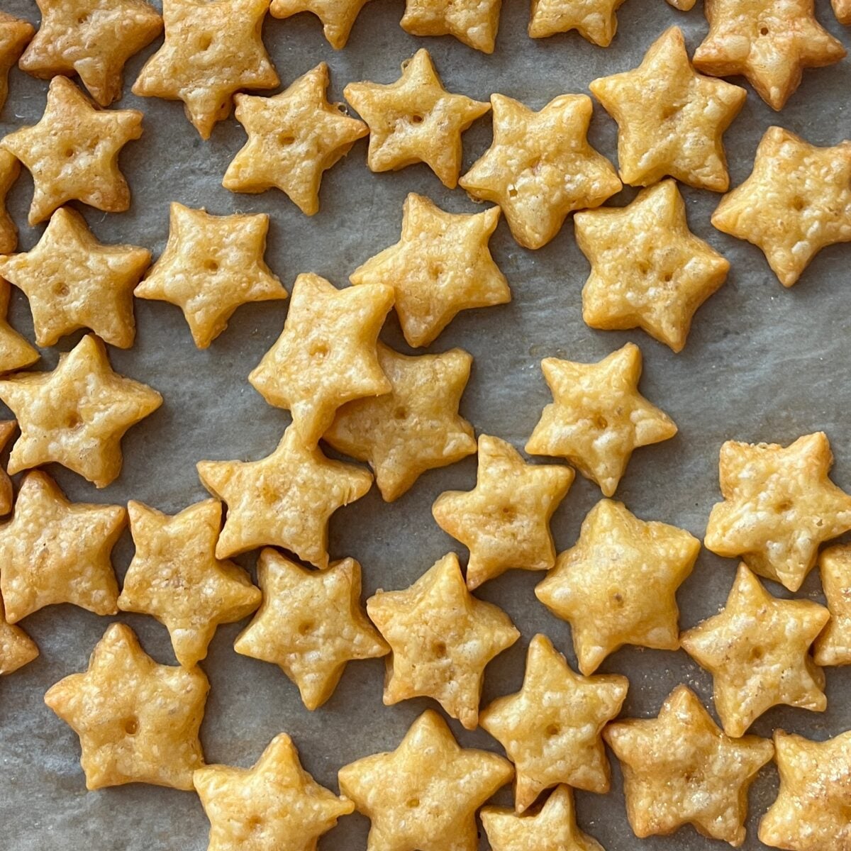 Several baked star-shaped Cheddar Crackers are spread across a sheet of parchment paper.