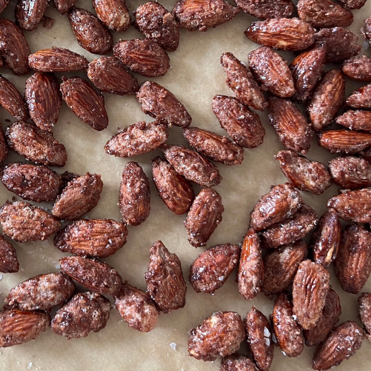 Close-up of candies almonds coated in a sugar mixture, scattered on a sheet of parchment paper.