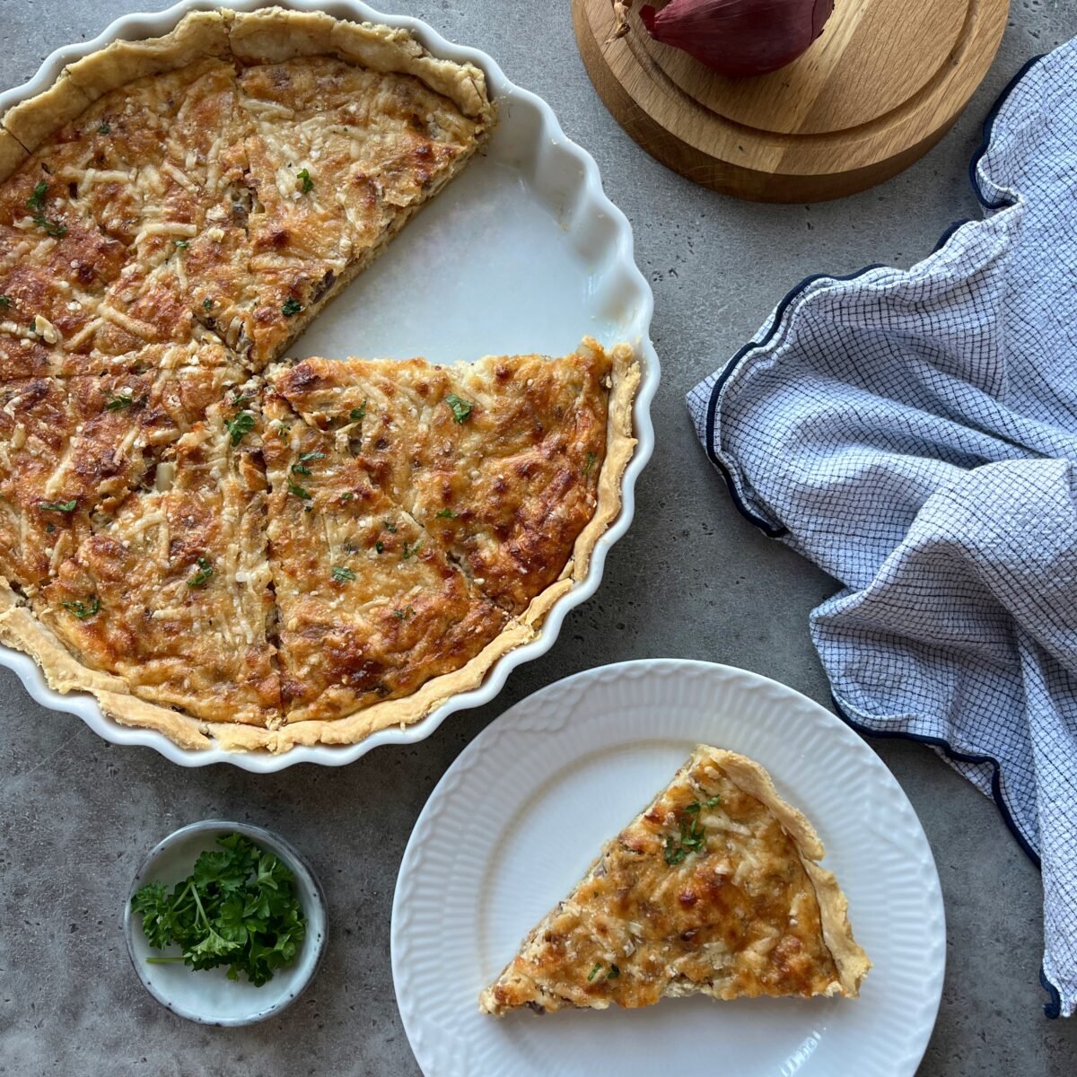 A baked Caramelised Onion Quiche with a slice removed sits in a ceramic dish.