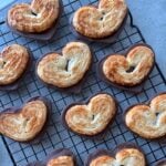 Heart-shaped puff pastries partially dipped in chocolate, arranged on a cooling rack over a gray surface.