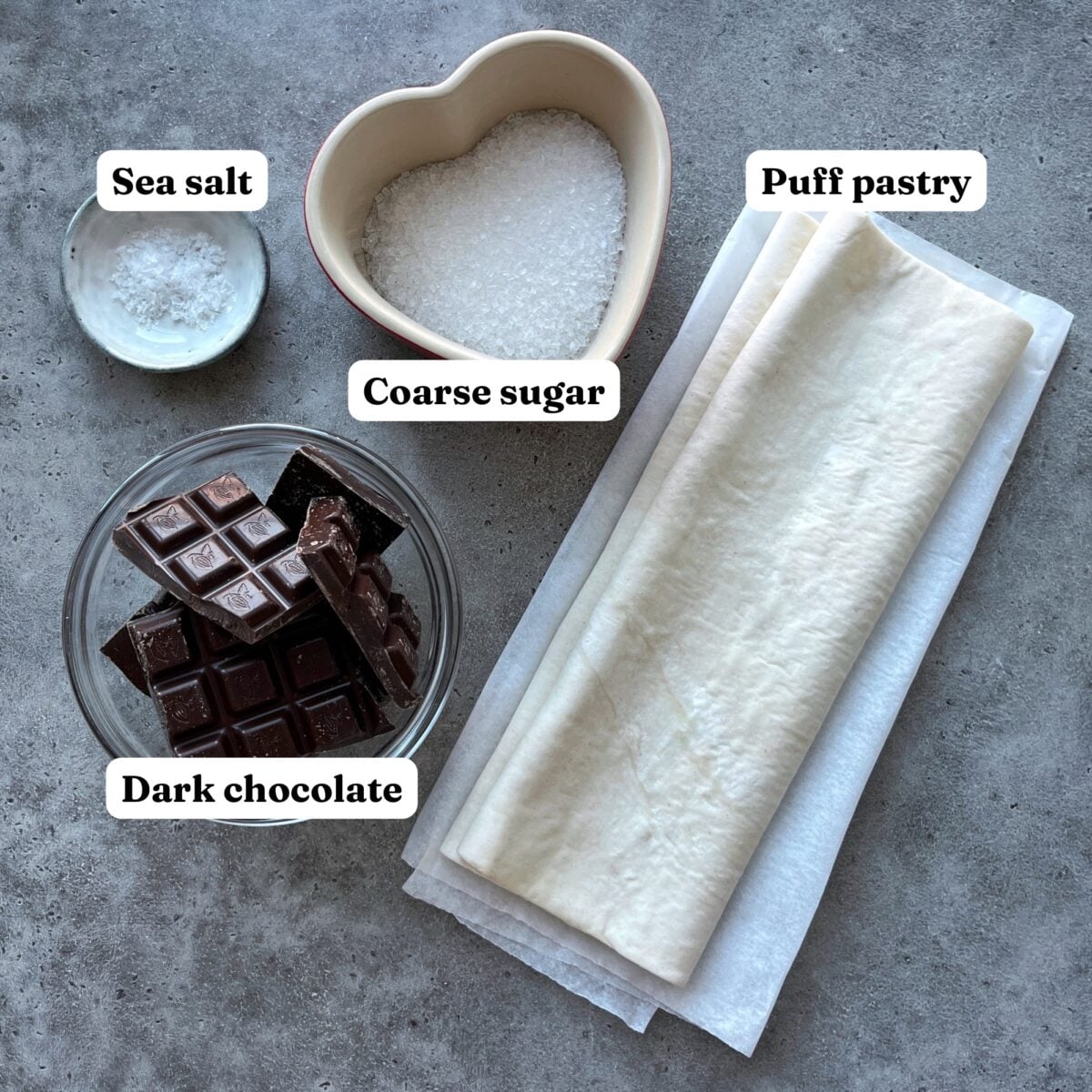 Puff pastry, dark chocolate, coarse sugar, and sea salt displayed on a grey surface.