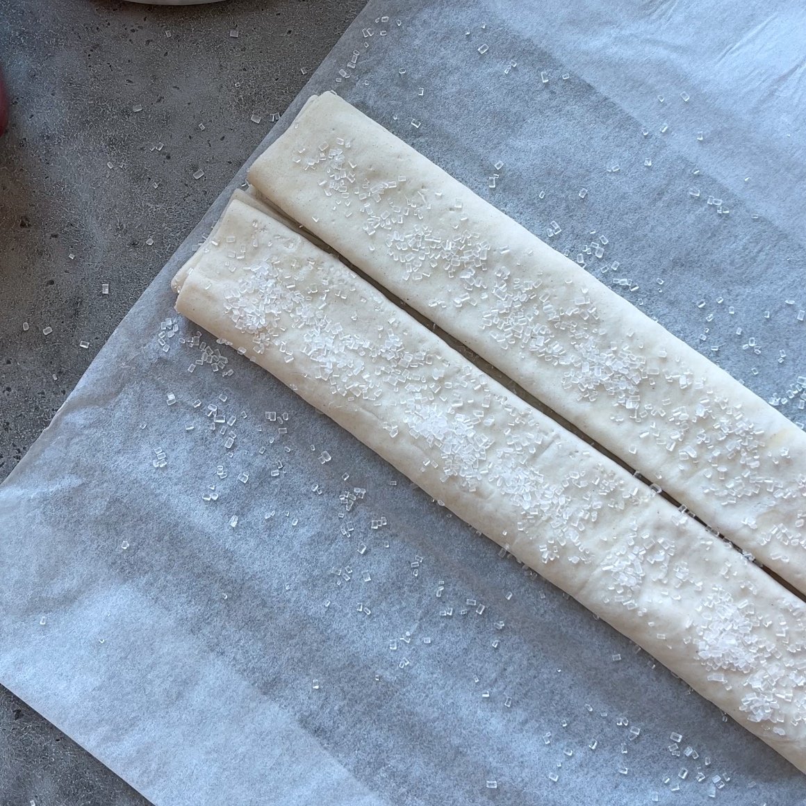 Rolled pastry dough sprinkled with coarse sugar rests on a sheet of parchment paper.