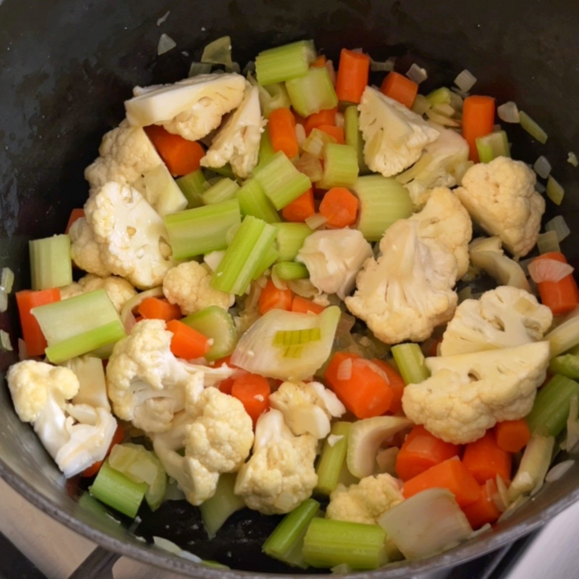 Chopped cauliflower, celery, carrots, and onions simmer together in a pot, creating the hearty base for a delicious Creamy Vegetable Soup.