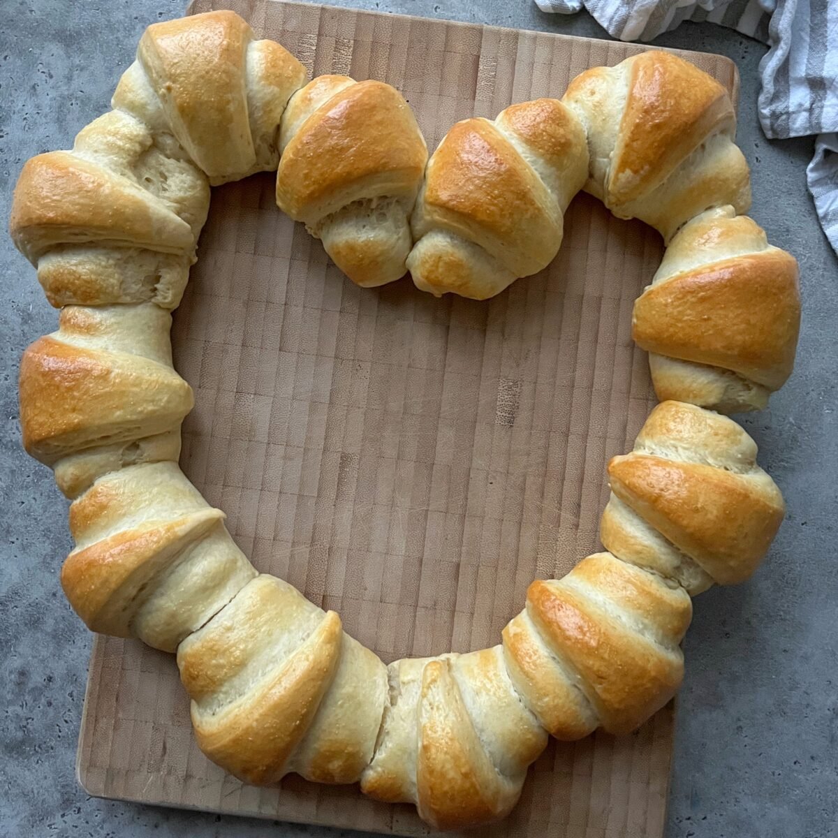 Golden-brown sausage rolls arranged in a heart shape on a wooden cutting board.