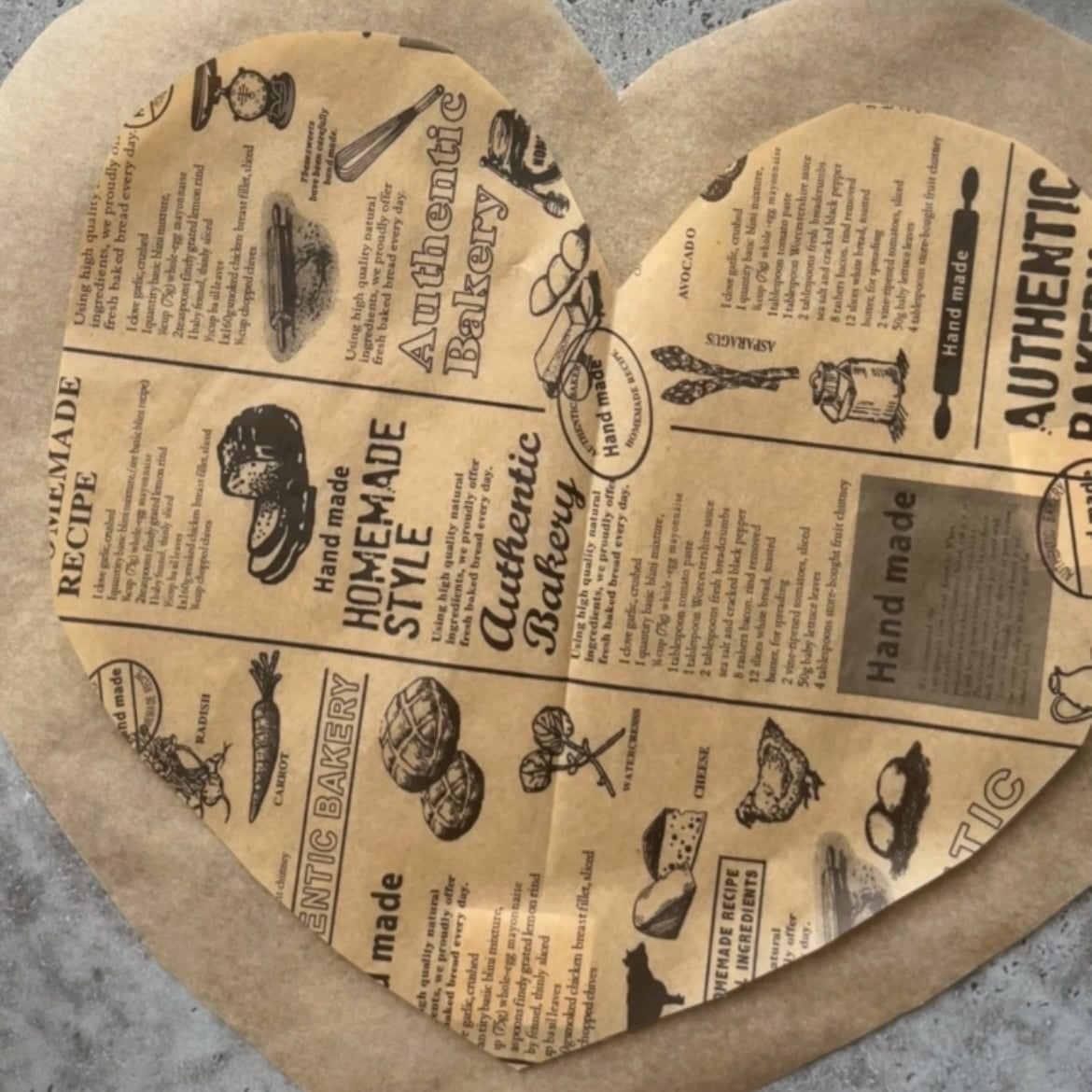 Heart-shaped piece of parchment paper printed with vintage-style bakery ads and illustrations.