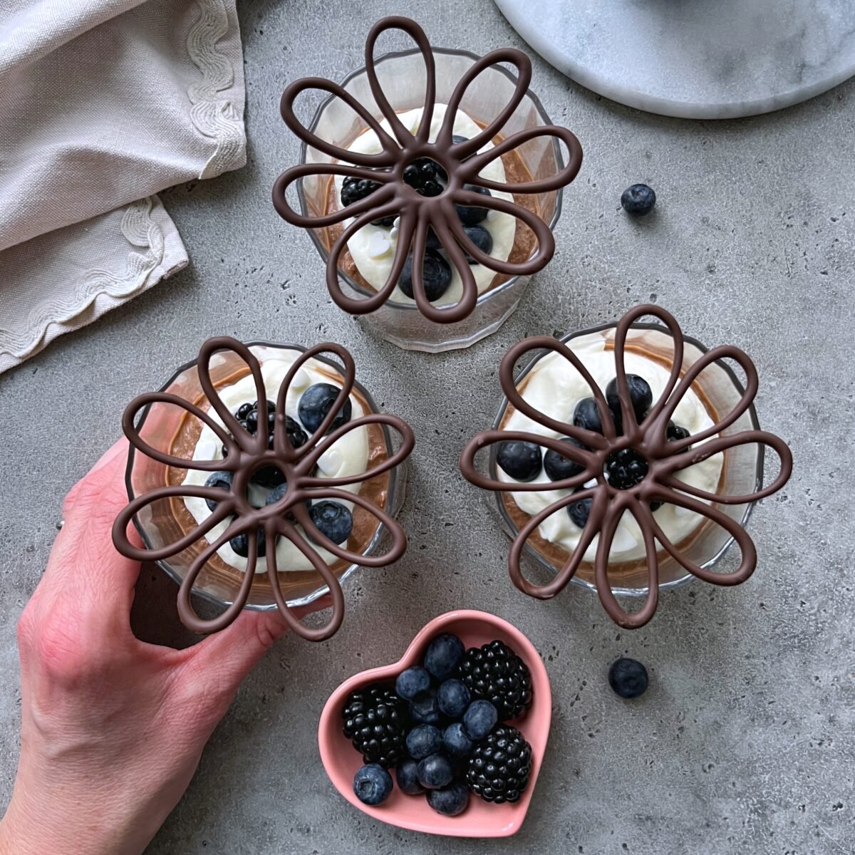 Three dessert glasses filled with chocolate mouse, whipped cream, berries, and decorative chocolate.