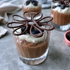 A glass of chocolate mousse topped with whipped cream, berries, and a decorative chocolate garnish.