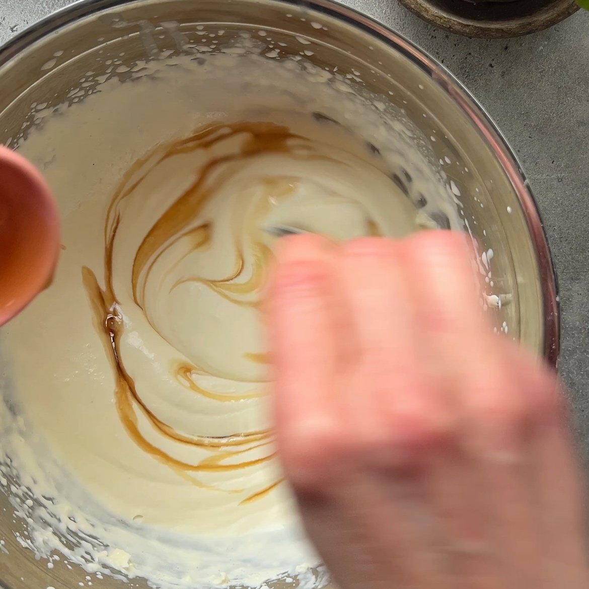 A hand stirs maple syrup into mascarpone whipped cream.